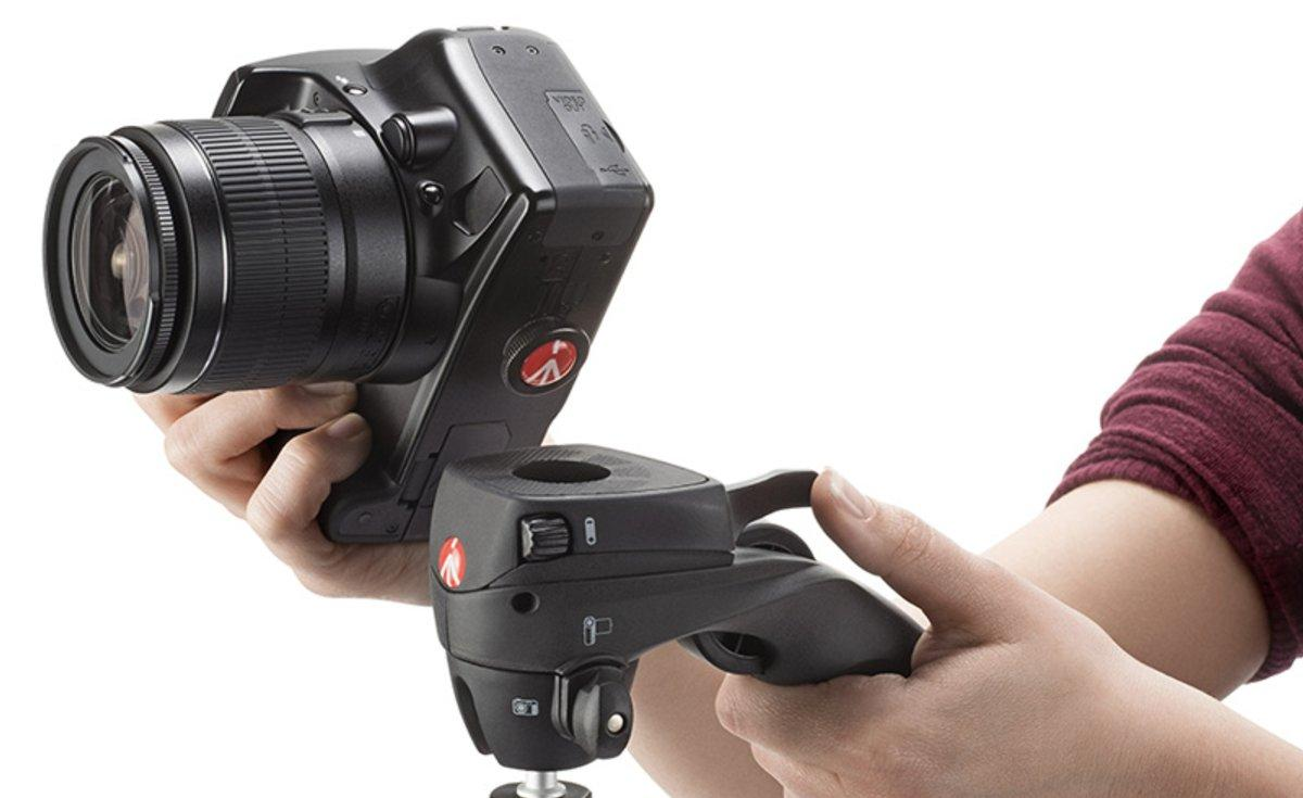 Mano de un fotógrafo sosteniendo una cámara conectada a una rótula, sobre fondo blanco.