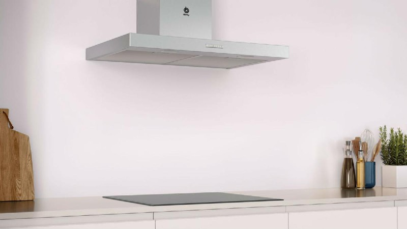 Una cocina blanca con una placa de cocina negra y una campana extractora plateada.
