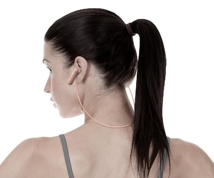 Mujer con coleta usando auriculares melocotón, vista desde atrás.