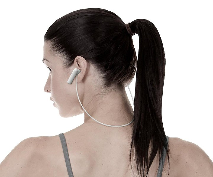 Mujer con coleta usando auriculares inalámbricos blancos, vista lateral, fondo blanco.