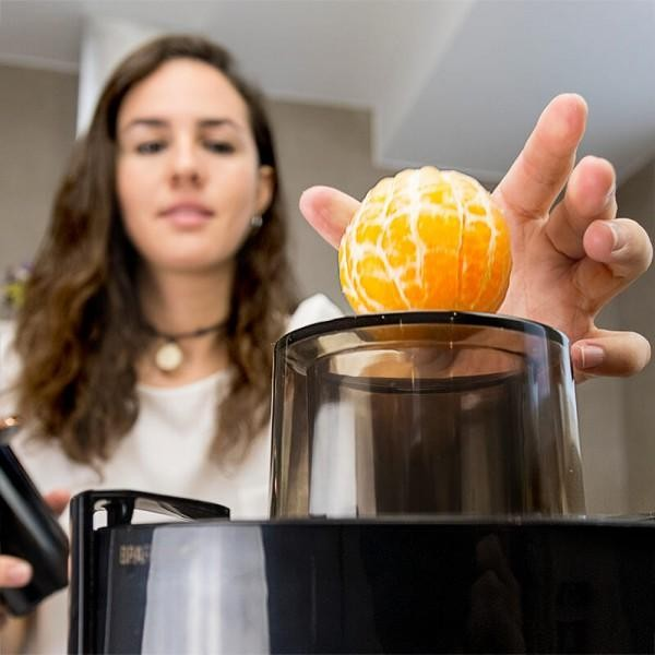Una mujer preparando una naranja para exprimirla. Sostiene la naranja sobre la exprimidora.