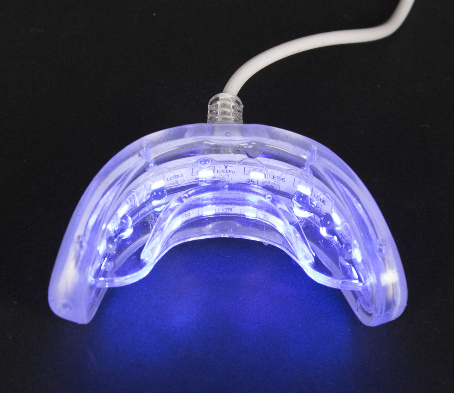 A clear, glowing blue LED teeth whitening device. White wire attached. Set against a black background.