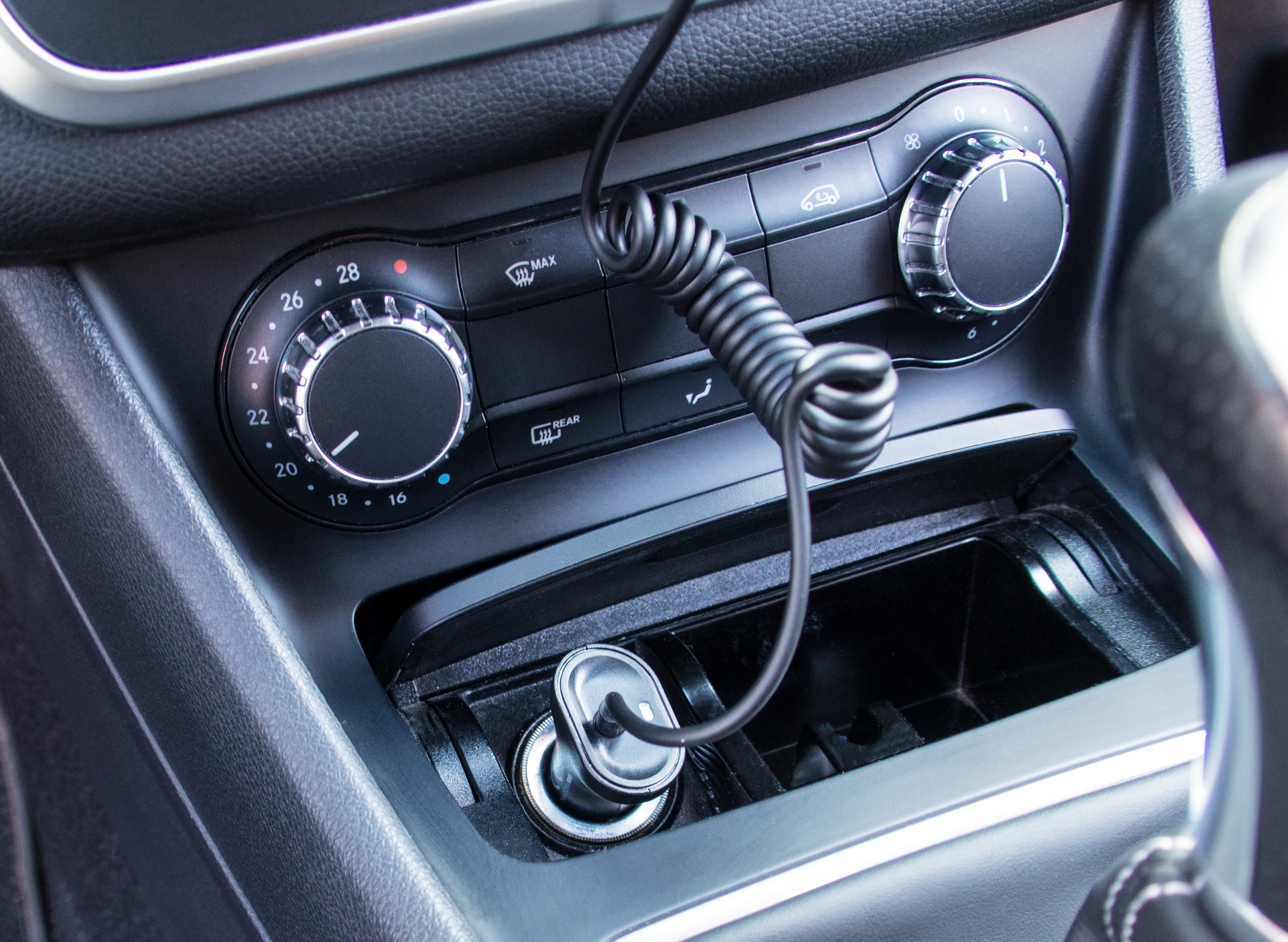 Nahaufnahme des Armaturenbretts eines Autos. Enthält Lüftungsschlitze, Klimaanlagenregler und einen Ladeanschluss.