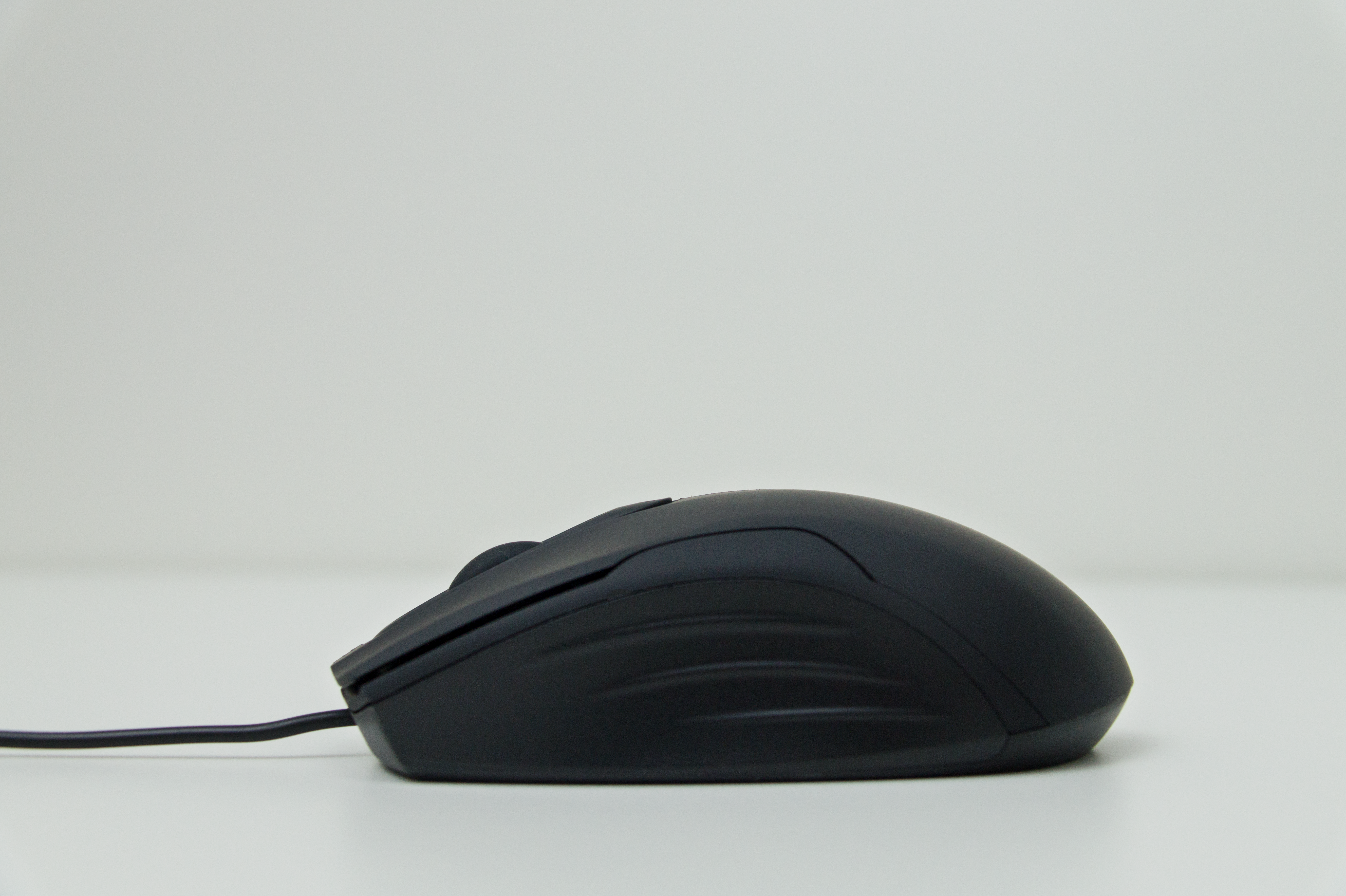Eine schwarze Computermaus auf weißer Oberfläche. Sie wird von der Seite betrachtet.