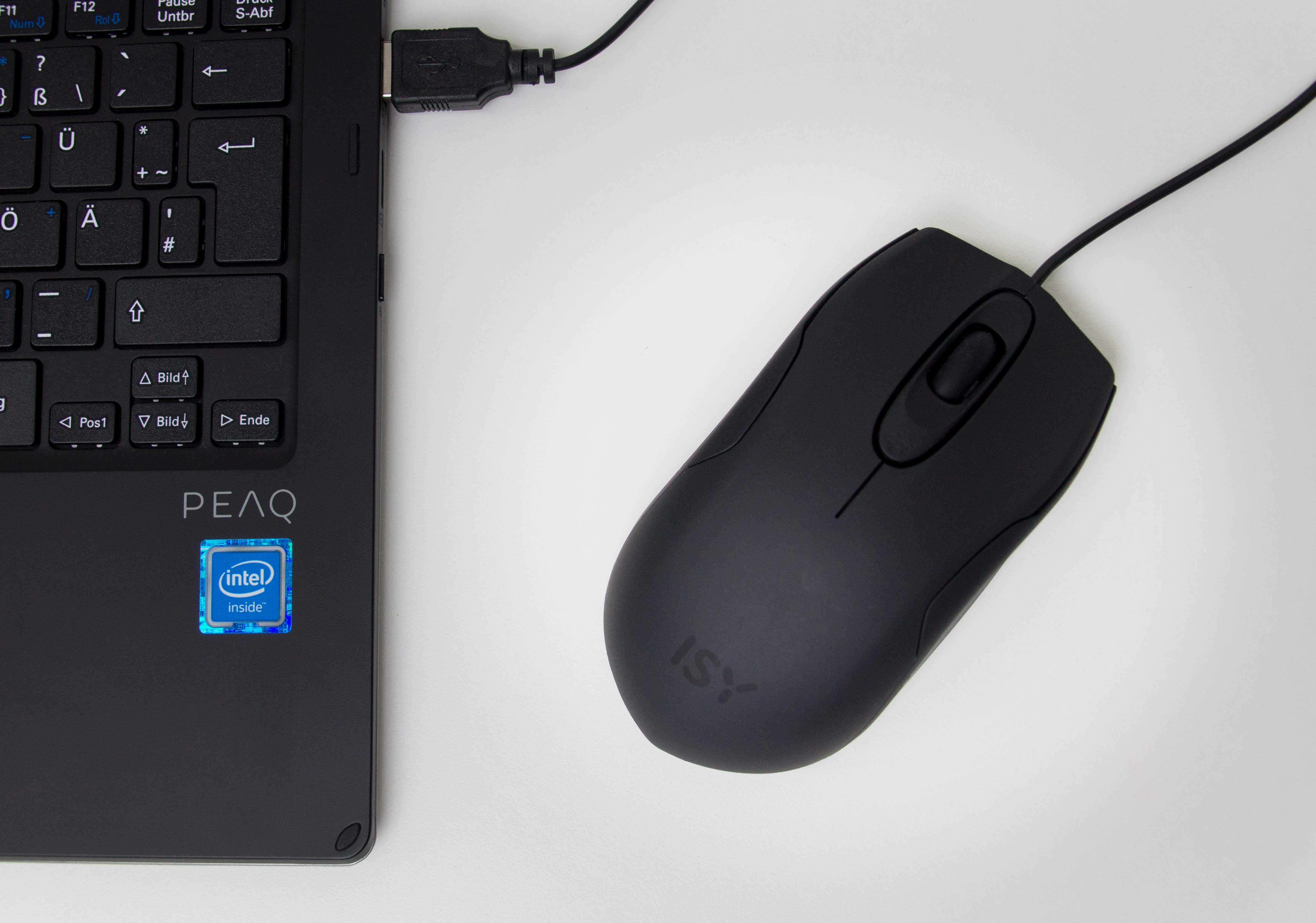 Schwarze Maus neben einem schwarzen Laptop. USB-Kabel angeschlossen. Weiße Oberfläche.