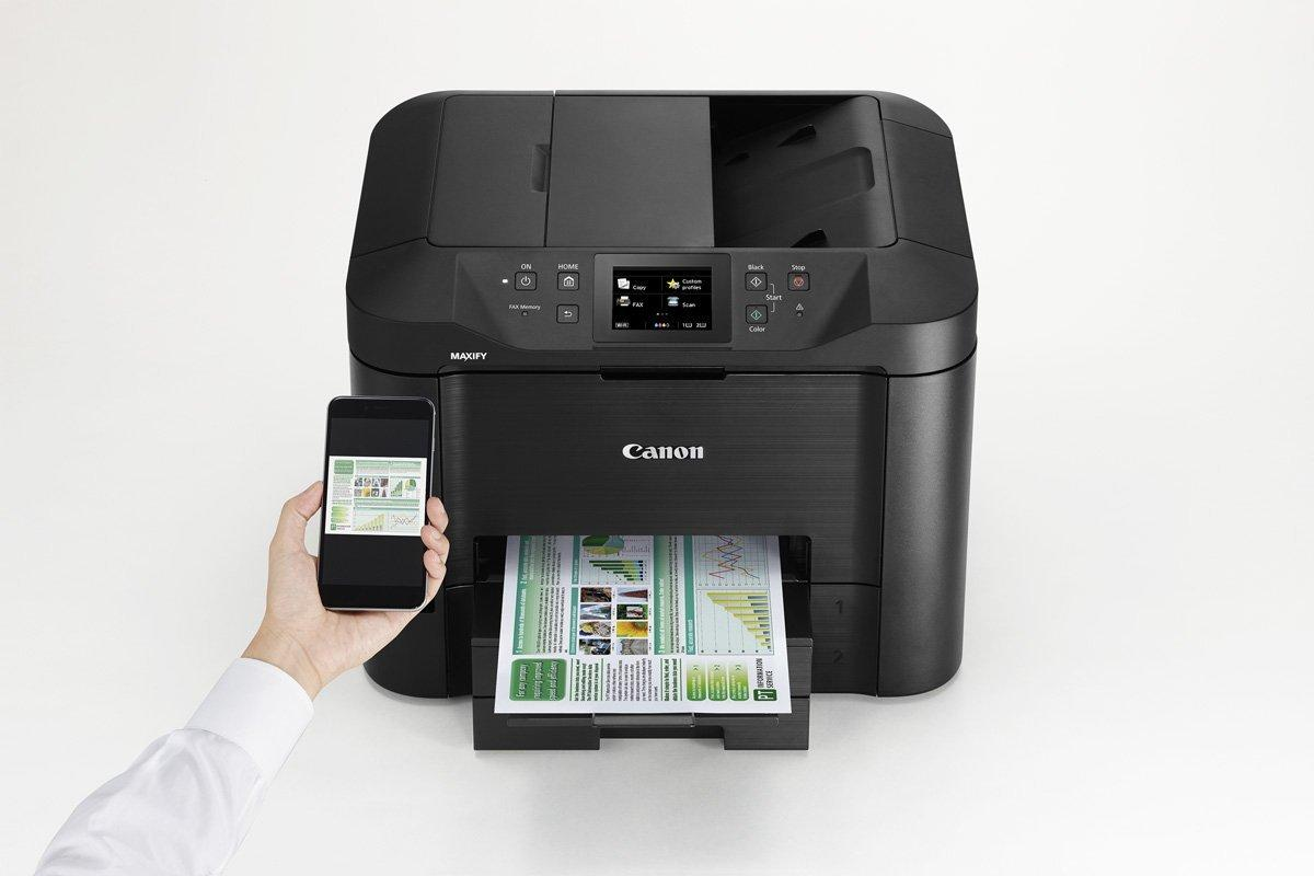 Una impresora Canon negra con un smartphone mostrando un documento. Papel impreso en la bandeja de salida.