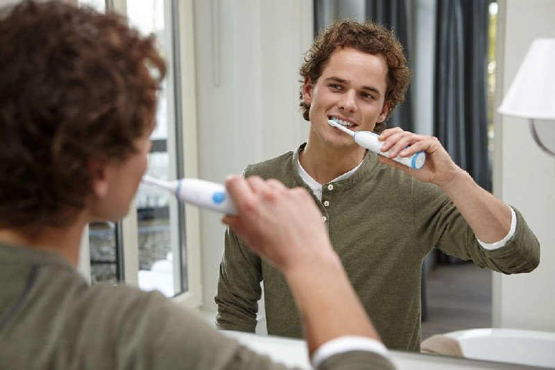 Un hombre cepillándose los dientes frente a un espejo, su reflejo es visible.