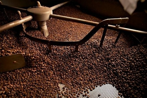 Primer plano de granos de café tostándose dentro de una máquina industrial metálica.