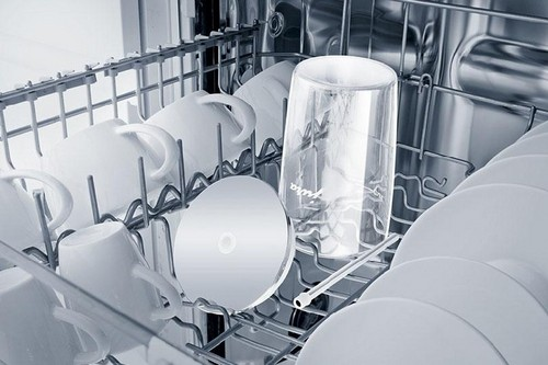 Interior de lavavajillas con tazas, vasos y platos blancos. Hay un CD. Estantes plateados.