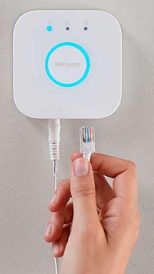 La mano de una persona sostiene un cable de red enchufado a un dispositivo blanco.