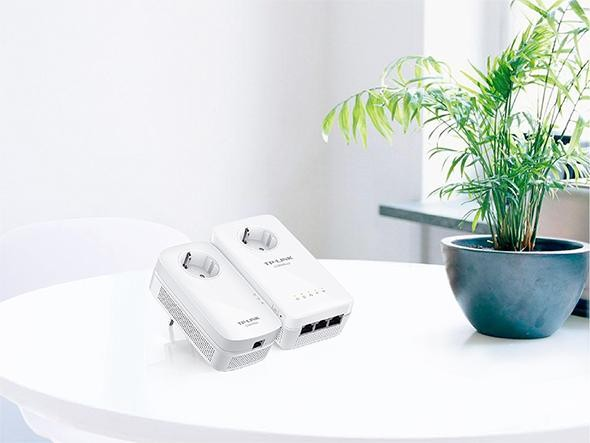 Dos adaptadores de línea eléctrica TP-Link blancos sobre una mesa. Una planta en una maceta oscura a la derecha.