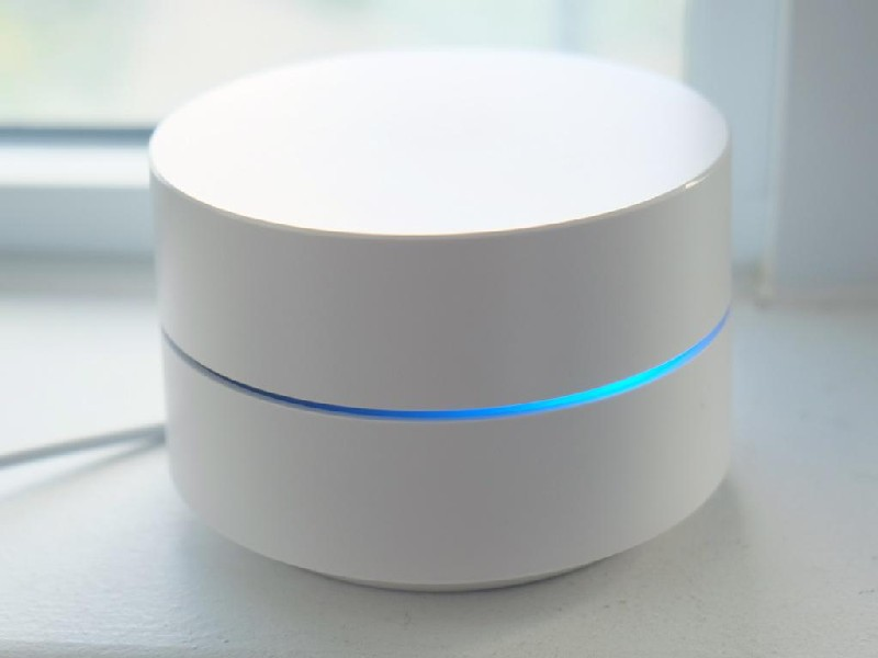 Enrutador Wi-Fi Google Nest blanco. Tiene una luz azul. El fondo es una ventana.