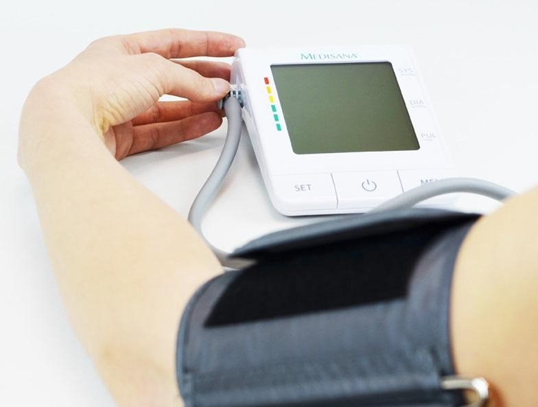 Brazo de una persona con un manguito de presión arterial. Un monitor de presión arterial blanco.