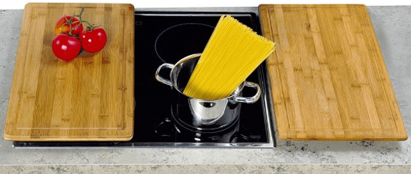 Espaguetis en una olla sobre una vitrocerámica negra, flanqueados por tablas de cortar.