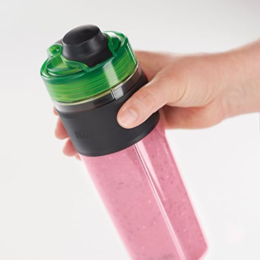 Mano sosteniendo botella de licuadora con batido rosa sobre fondo blanco.
