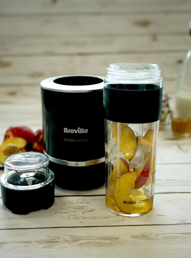 Licuadora Breville negra con un recipiente transparente con rodajas de durazno y hielo. Un pequeño recipiente con cuchillas es visible.