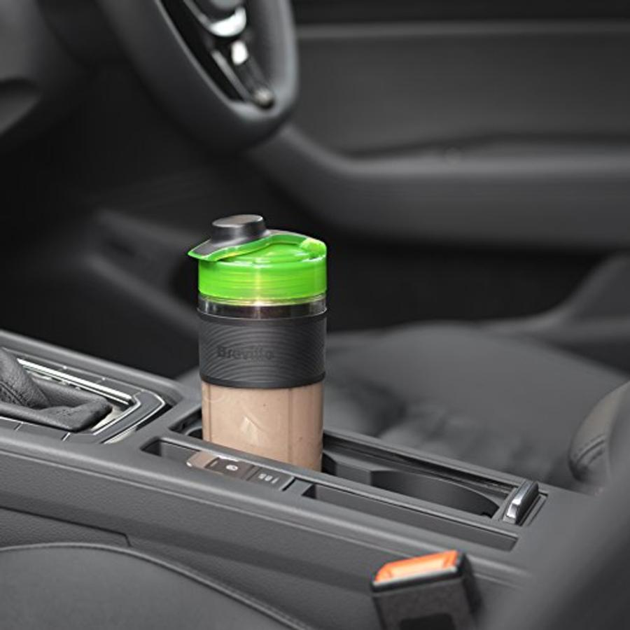 Un vaso de batido en el portavasos de un coche. La taza es verde y negra.