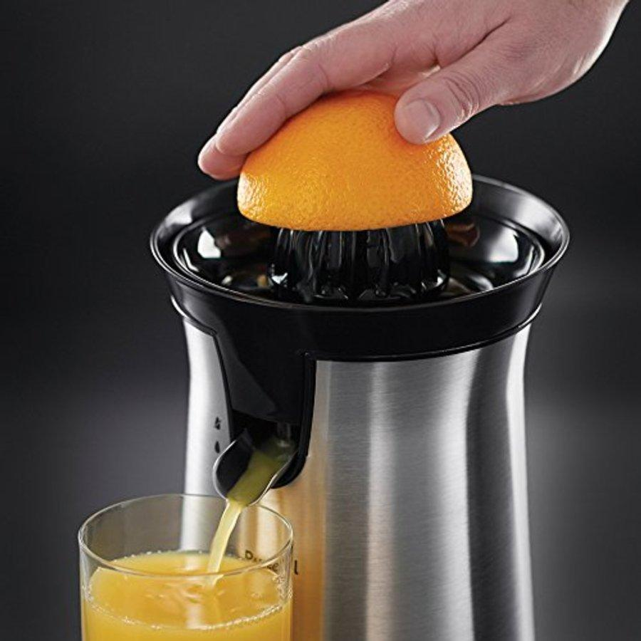 Mano exprimiendo media naranja en exprimidor. Jugo fluyendo a un vaso.