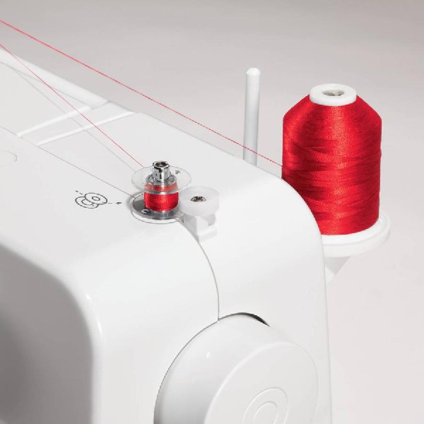 Máquina de coser blanca con carretes de hilo rojo. El hilo va de los carretes a la aguja. Primer plano.