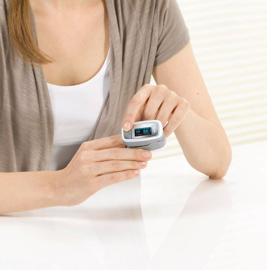 Persona sosteniendo un oxímetro de pulso mostrando lecturas.