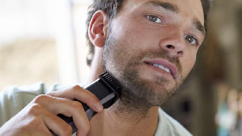Un hombre se afeita la barba con una recortadora eléctrica negra. Su rostro está en primer plano y enfocado.