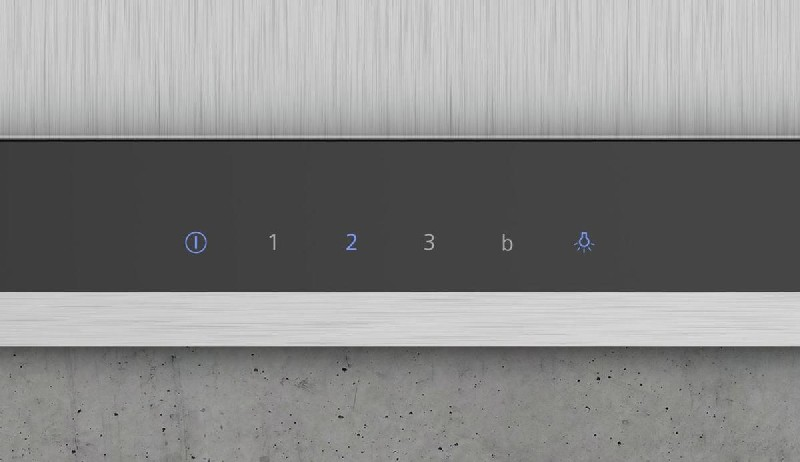 Primer plano de un panel de control negro con botones: encendido, ajustes y luz, sobre superficie gris.