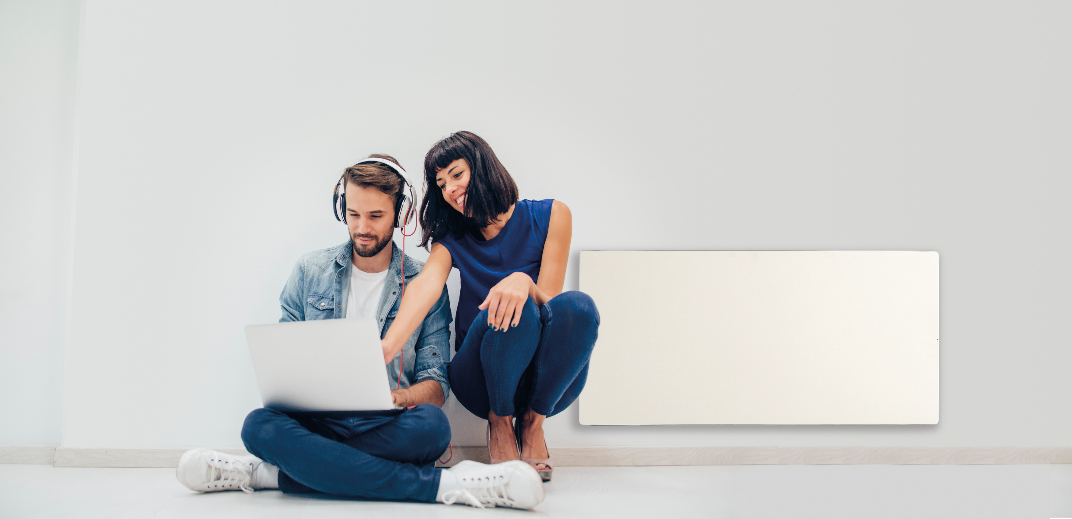 Ein Paar sitzt an einer weißen Wand mit Laptop und Wandheizung.
