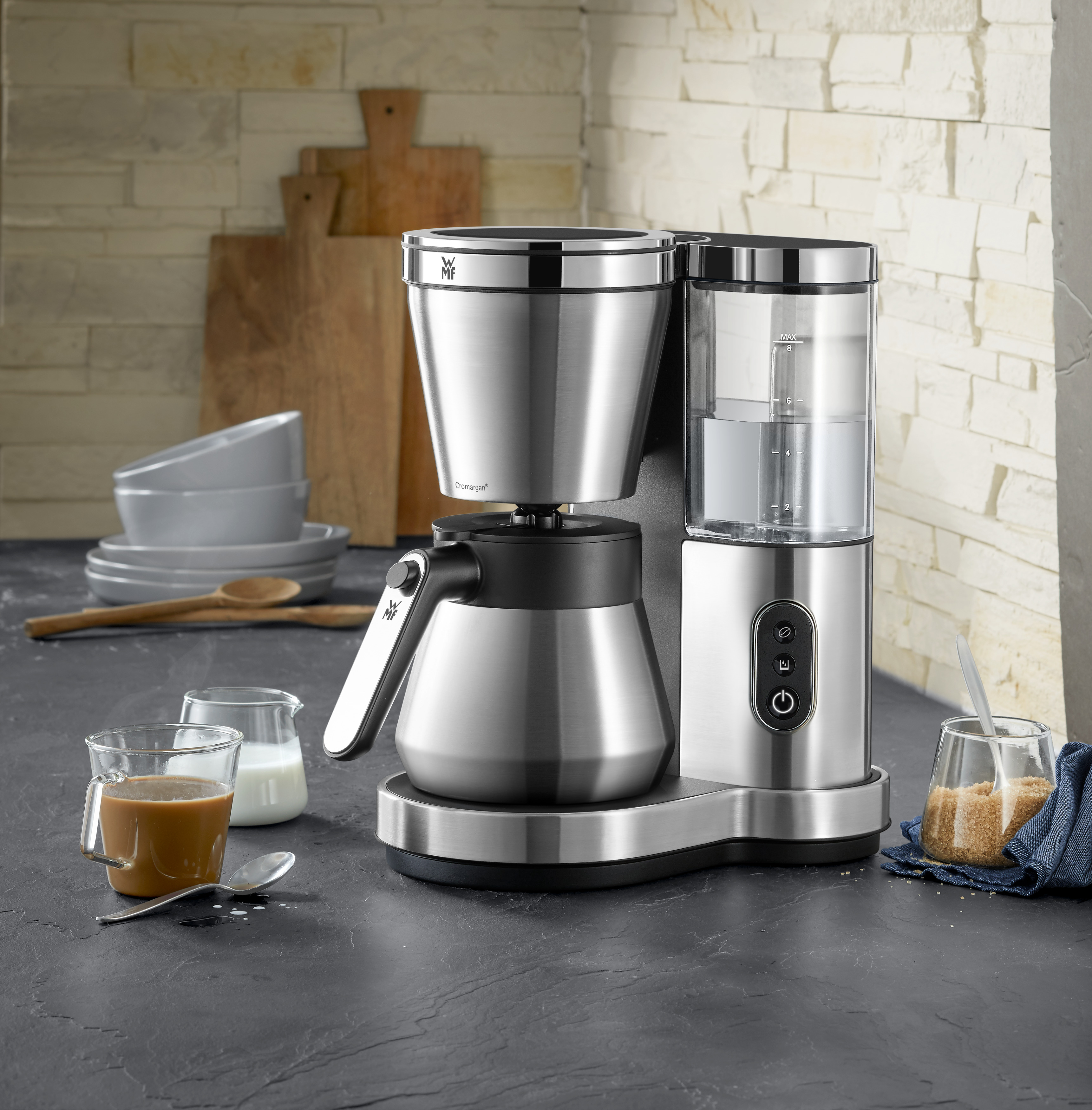 Eine Kaffeemaschine aus Edelstahl auf schwarzer Oberfläche, mit Kaffee, Milch und Zucker.