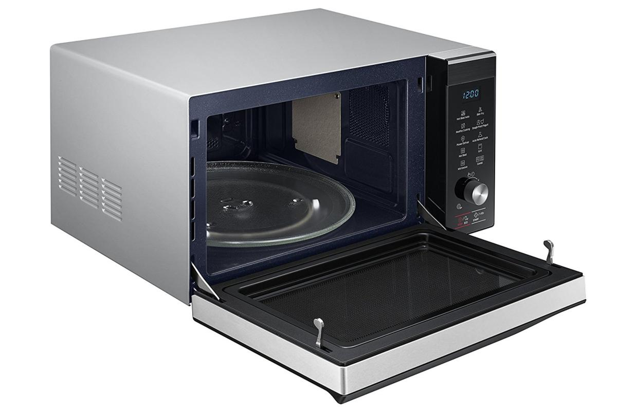 Un horno de microondas con la puerta abierta. Dentro hay un plato de cristal y una bandeja negra.