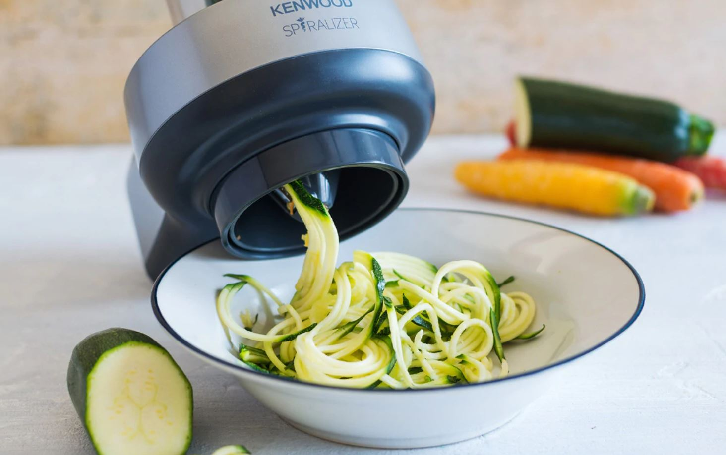 Un spiraliseur coupe des courgettes en nouilles, avec des courgettes et des carottes en arrière-plan.