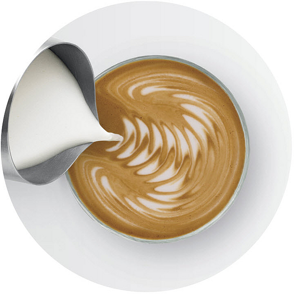 Latte Art in einer Tasse, Sahne wird aus einem Metallkrug gegossen.