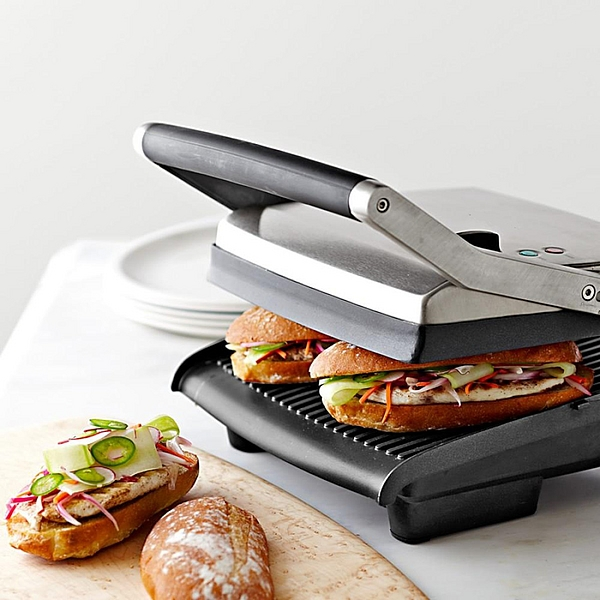 Sandwiches auf einer Panini-Presse, eines offen mit sichtbaren Belägen, auf einem Holzbrett.