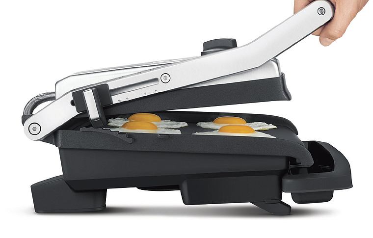 Grill mit gebratenen Eiern. Eine Hand hebt den oberen Teil des Grills an.
