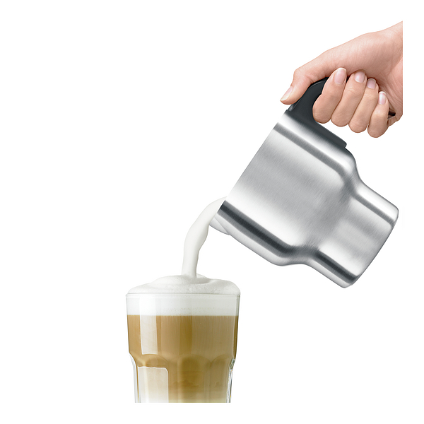 Hand gießt geschäumte Milch in ein Glas Latte. Milch ist weiß. Glas ist im Fokus.