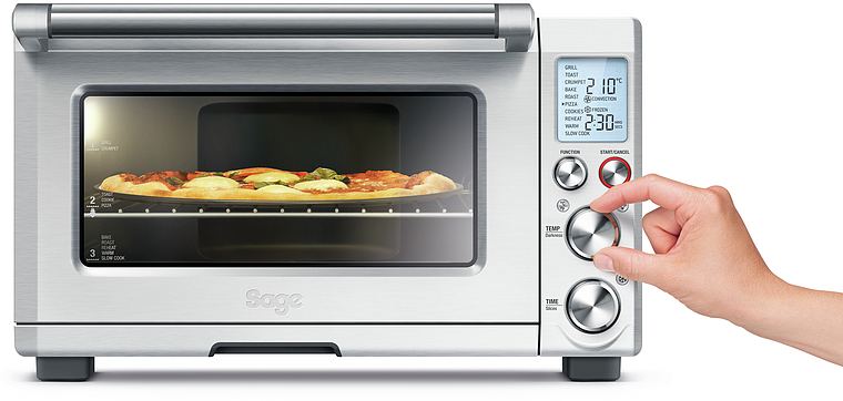Silberner Backofen mit Pizza. Eine Hand stellt den Temperaturregler ein.