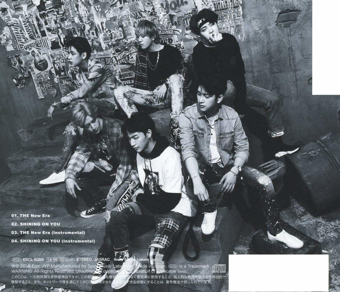 Six young men in casual attire pose together. The background features graffiti-covered walls and a dark, urban setting.