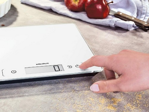 La mano de una persona presionando un botón en una balanza de cocina digital blanca.