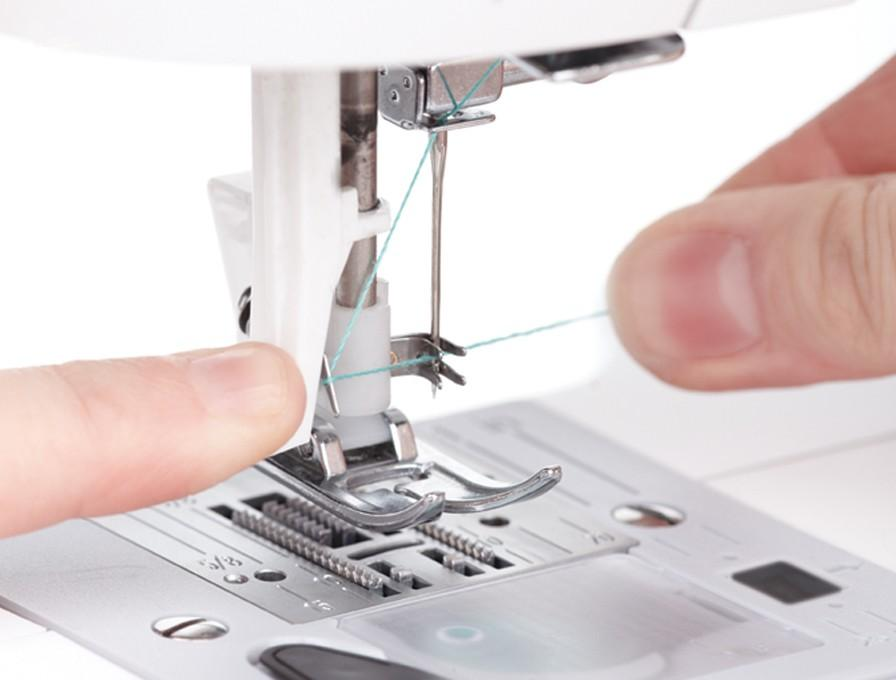 Primer plano de una máquina de coser. Una persona está enhebrando la aguja con hilo verde claro.