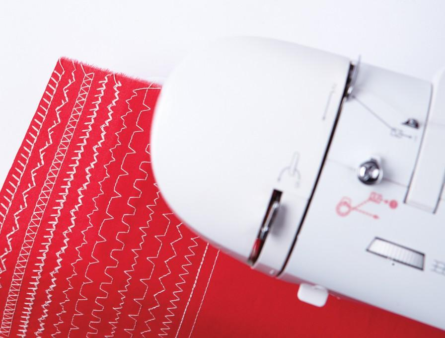 Tela roja con patrones de costura blancos, cerca de una máquina de coser.