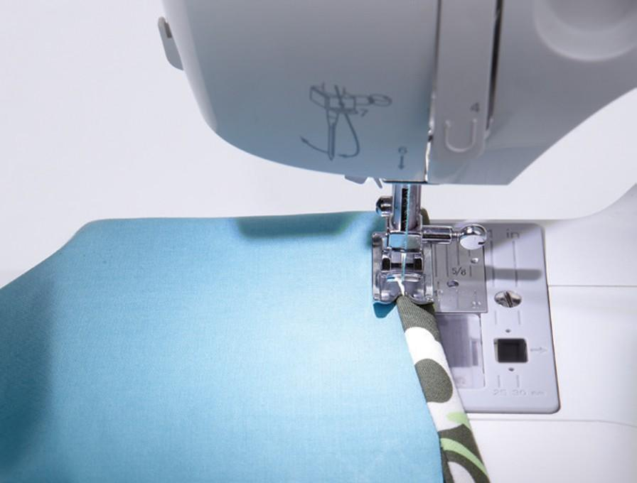 Una máquina de coser en acción. Se cose tela azul con un borde estampado en verde y blanco.