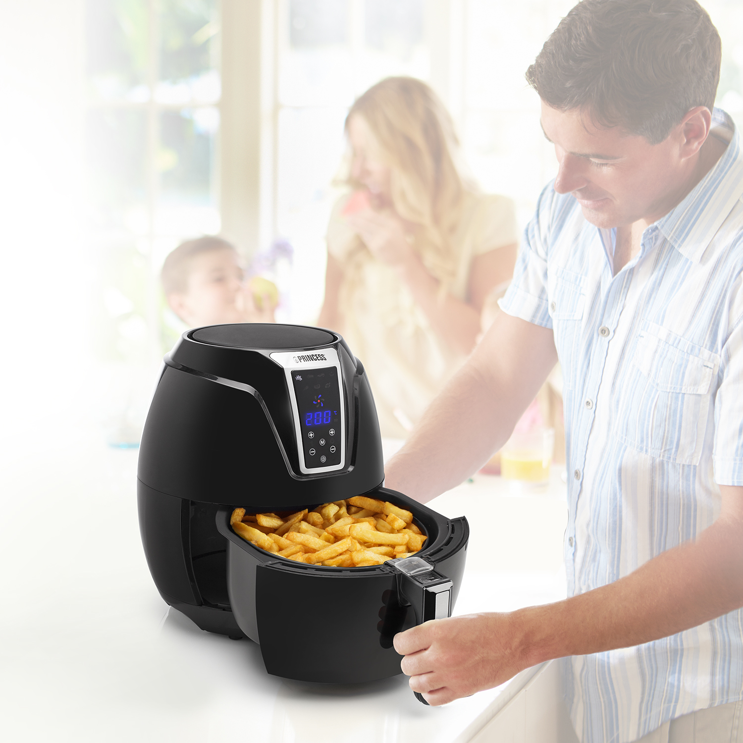 Hombre usando freidora de aire negra, con papas fritas en la cesta, familia detrás.