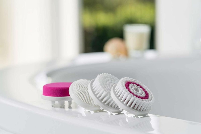 Cuatro cepillos de limpieza facial sobre superficie blanca, varios colores y texturas, fondo desenfocado.