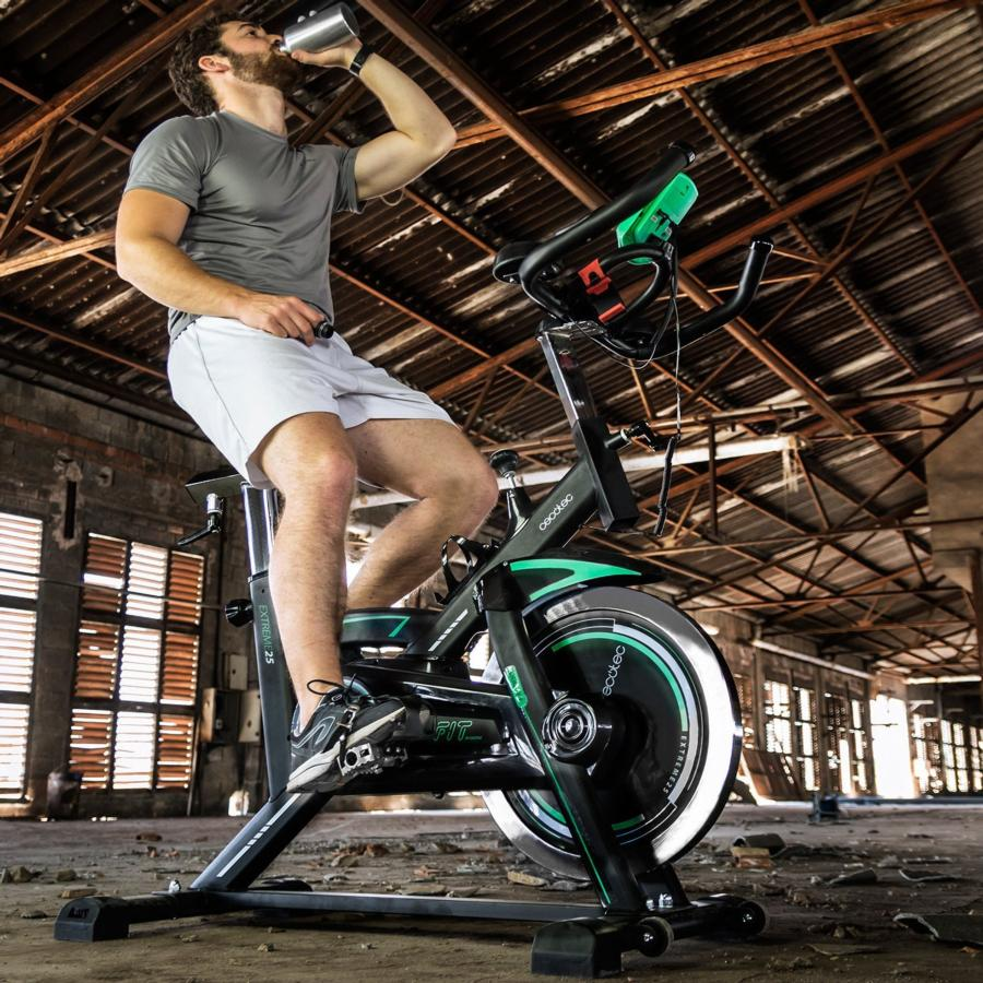 Hombre bebiendo agua en bicicleta estática. Camiseta gris y pantalones cortos blancos. Gimnasio.
