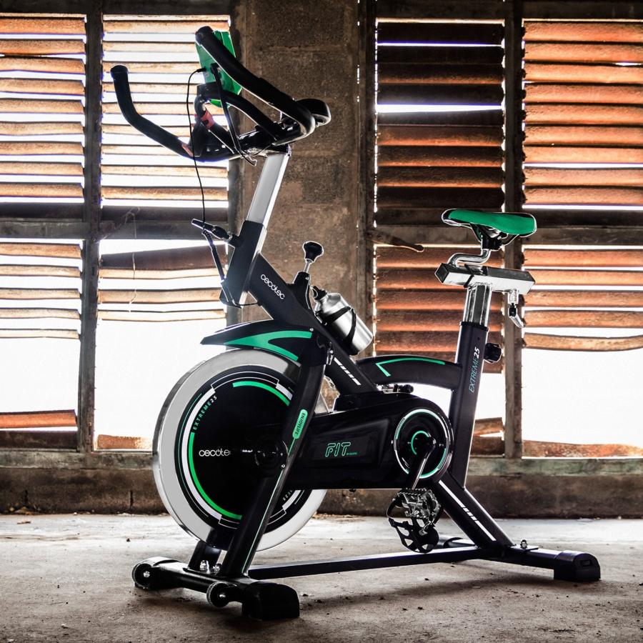Bicicleta estática con marco negro, detalles verdes y rueda blanca, frente a una ventana.