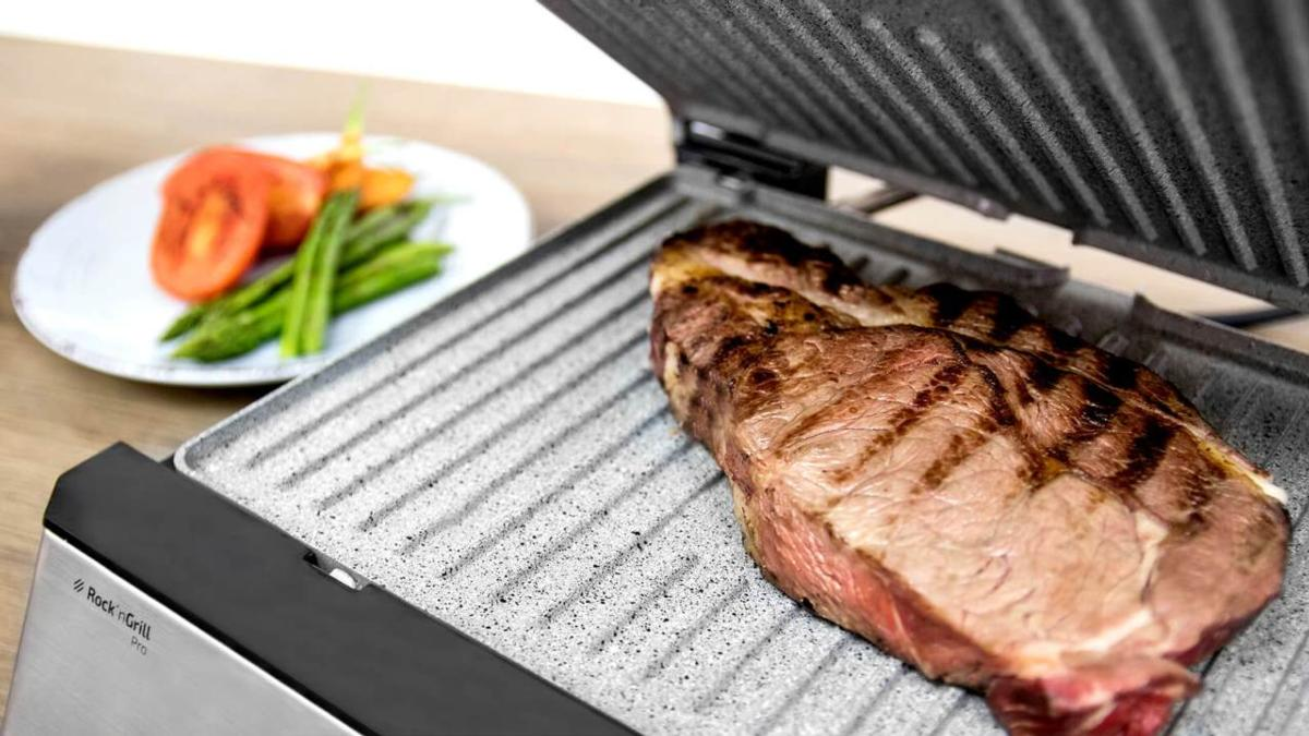 Un bistec a la parrilla en una parrilla con un plato de verduras al lado.