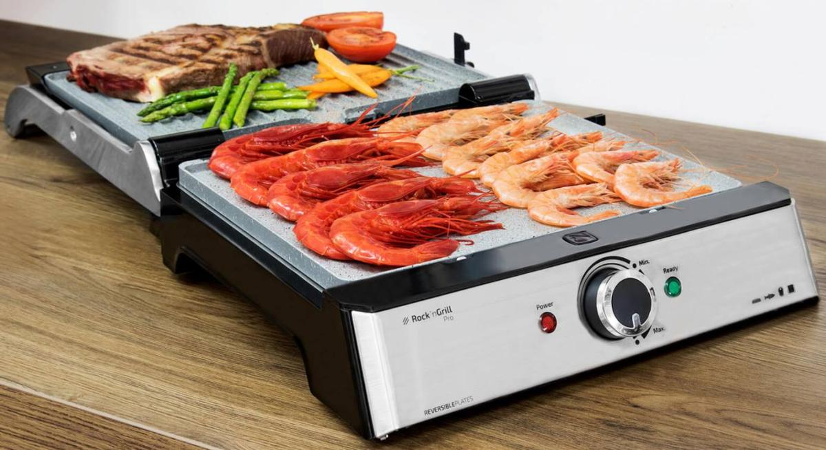 Parrilla con bistec cocido, verduras y camarones. La parrilla está sobre una mesa de madera.