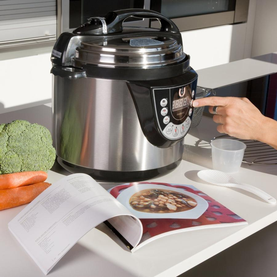Olla a presión con comida y libro de cocina en mostrador blanco.
