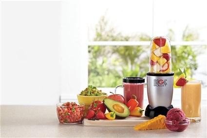 Licuadora con frutas y verduras en un mostrador. Hay cuencos de salsa y guacamole.