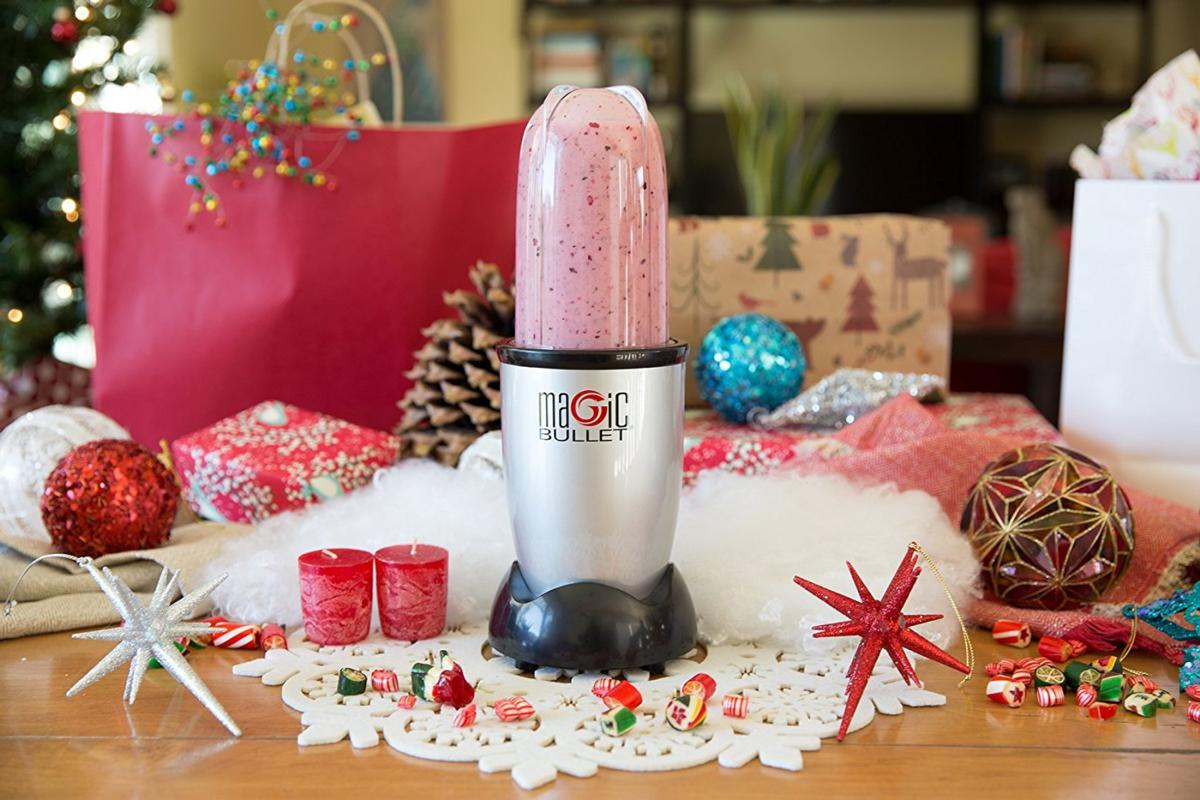 Licuadora Magic Bullet con un batido rosa, sobre una mesa con decoraciones navideñas.