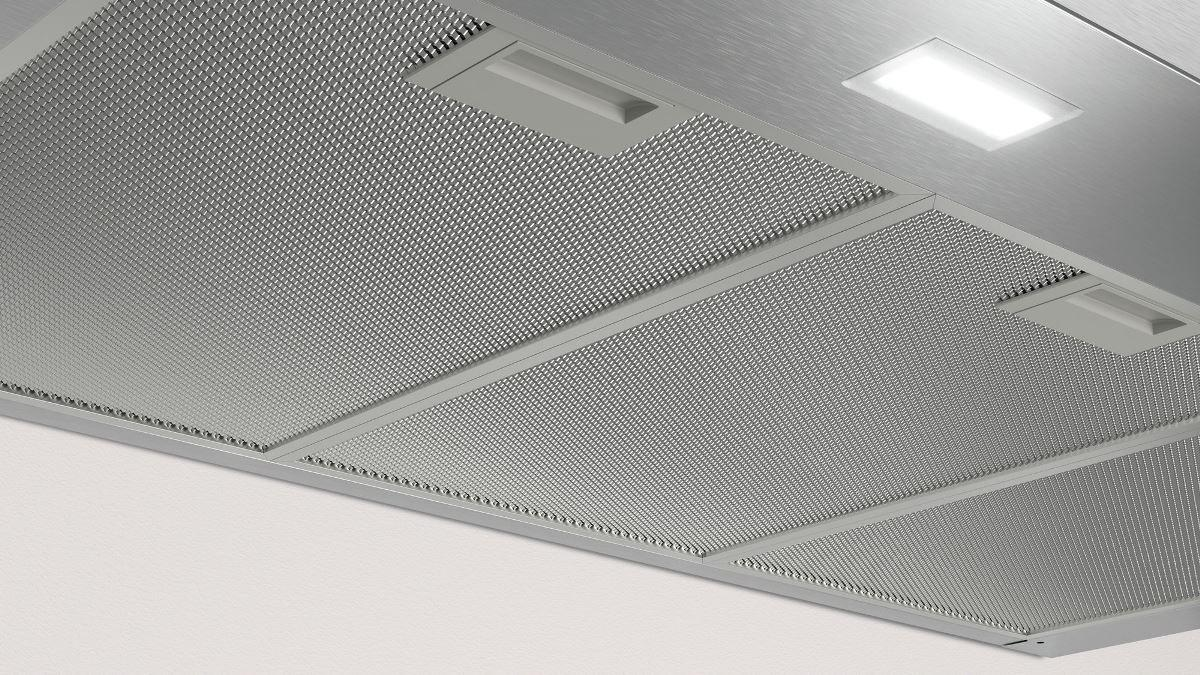Primer plano de una campana extractora de cocina. Es de metal con un patrón de rejilla y una luz integrada.